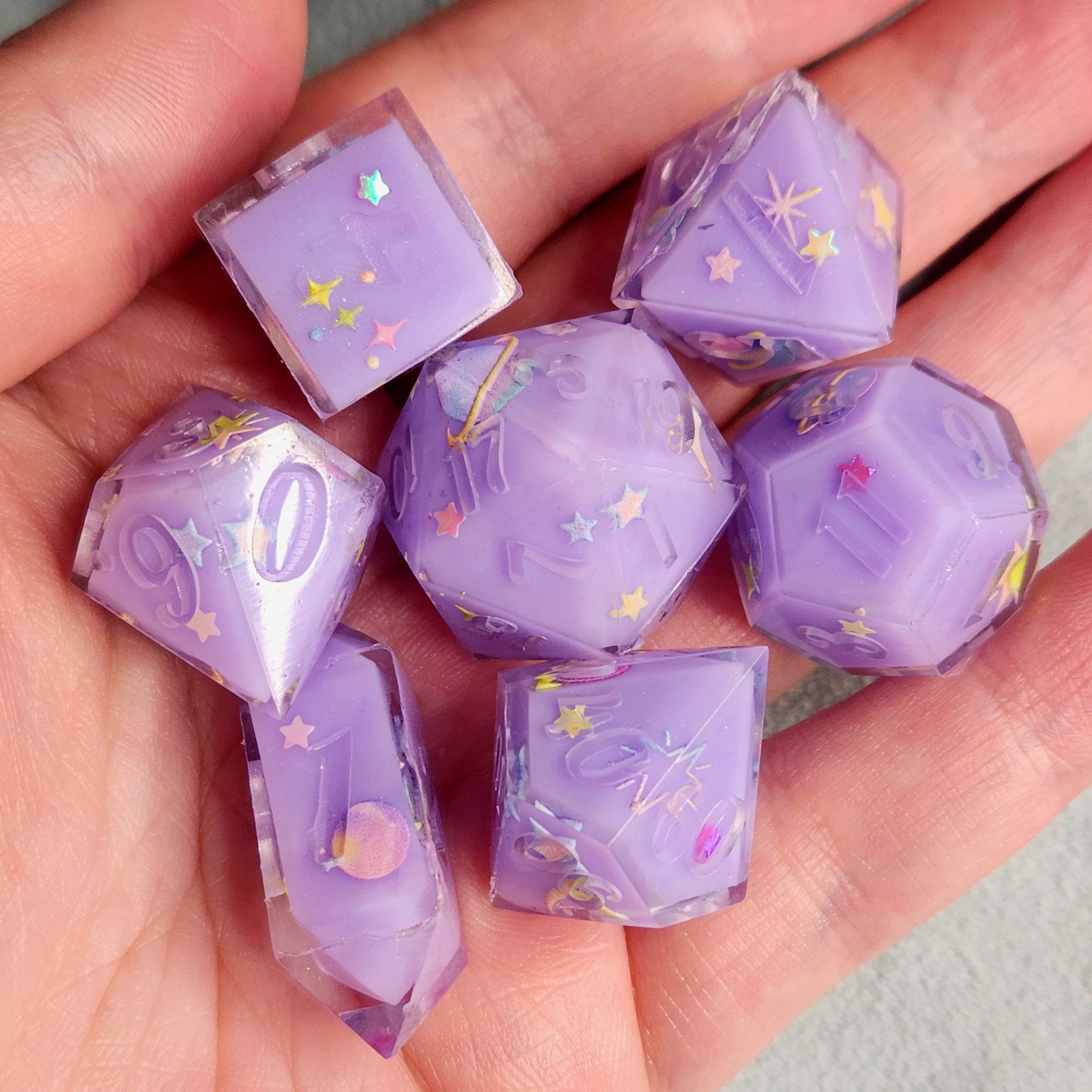 Purple dice with star and fairy designs held in a hand against a neutral background